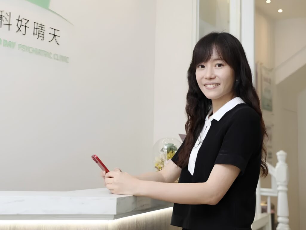 Smiling woman in a black dress at a marble reception desk, signing with a red pen at the counter.