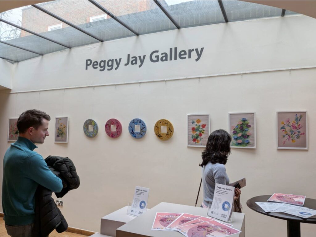 Gallery interior with a 'Peggy Jay Gallery' sign and visitors viewing botanical prints on a beige wall