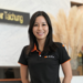 Smiling woman in a black polo with orange trim standing in a reception area with a Victor Taichung sign in the background.